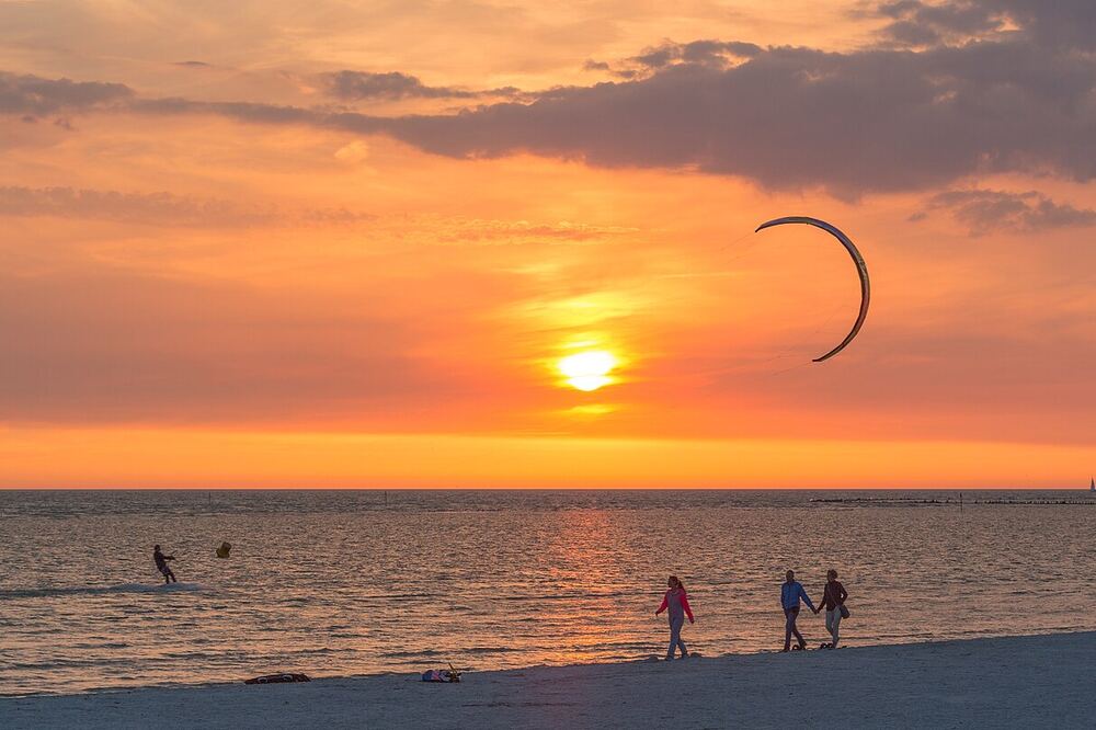 Zonsondergang boven het IJsselmeer bij Workum, met een kitesurfer op het water en wandelaars op het strand