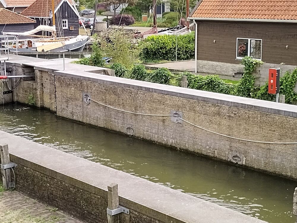 Schutsluis in Workum met een klassiek zeilschip en houten huizen aan het water erachter